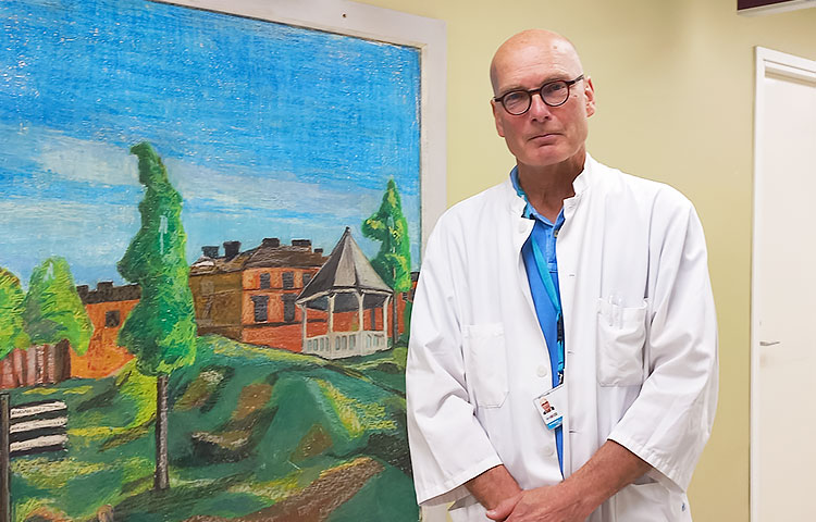 Mies lääkärintakissa seisoo käytävällä maalauksen vieressä.
