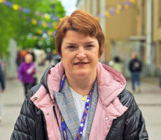 Lähikuva naisesta, taustalla kaupunki ja ihmisiä.