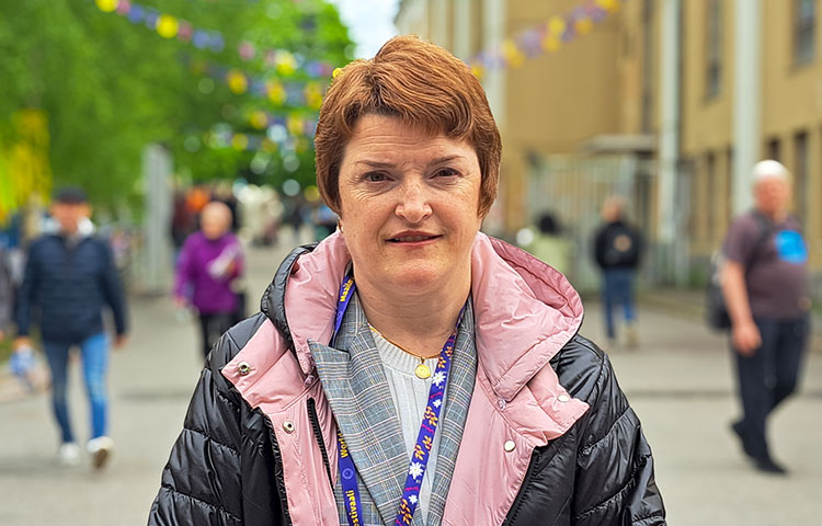 Lähikuva naisesta, taustalla kaupunki ja ihmisiä.