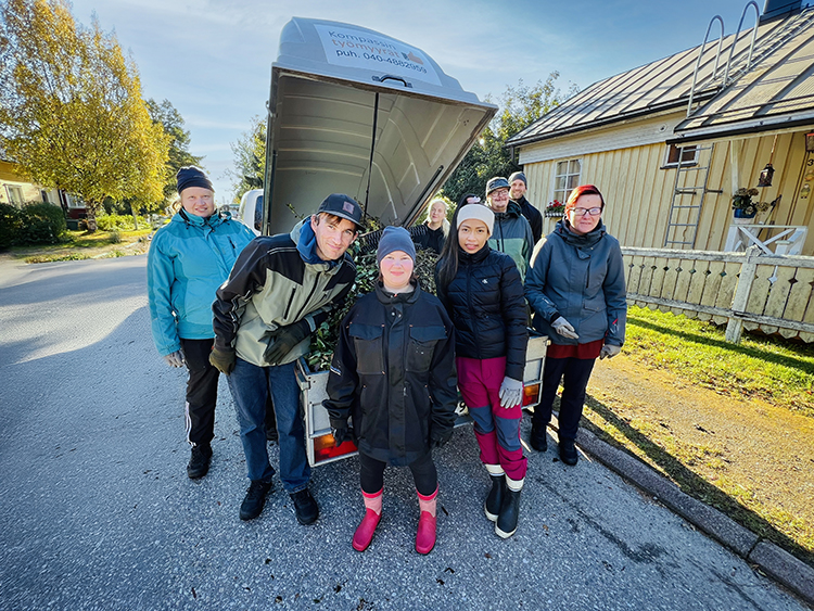 Työporukka ryhmäkuvassa avonaisen peräkärryn lavan edessä.