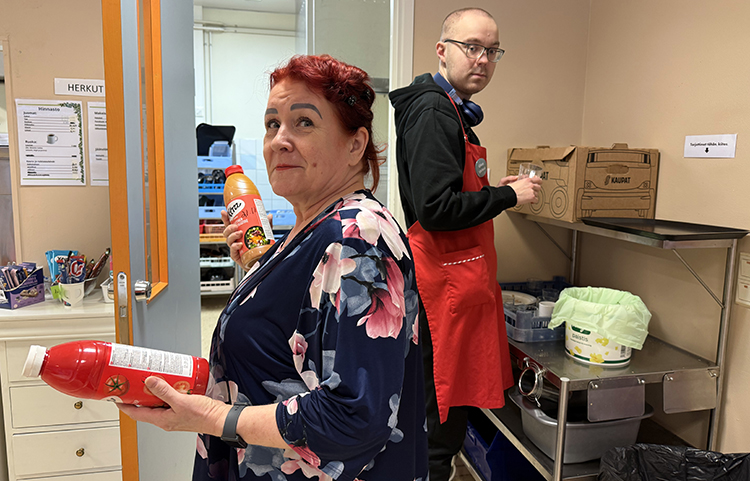 Kaksi henkilöä keittiössä, toisella kädessä ketsuppipullo ja toinen on taaempana kierrätysastioiden vieressä.