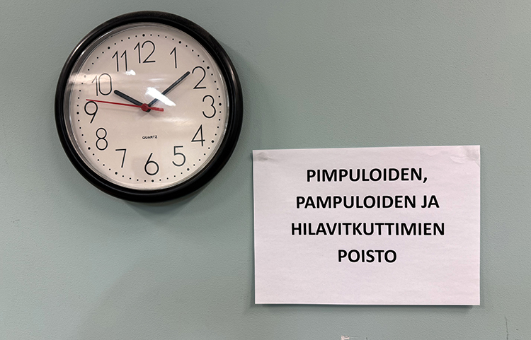 Kellotaulu ja sen vieressä lapulle kirjoitettu teksti: Pimpuloinen, pampuloiden ja hilavitkuttimien poisto.