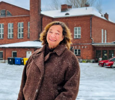 Kuvassa Outi Airola, taustalla punatiilinen rakennus.