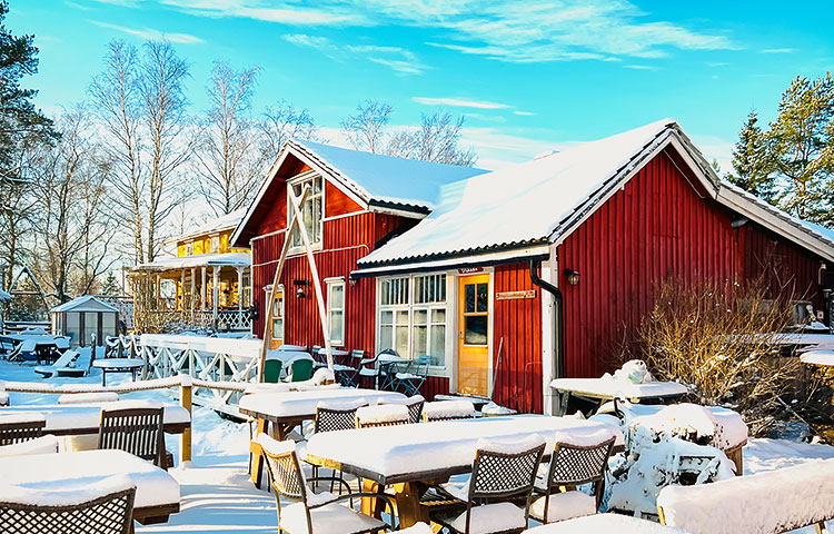 Kuva talvisesta pihapiiristä, punainen puutalo ja sen etualalla lumen peittämiä terassikalusteita.