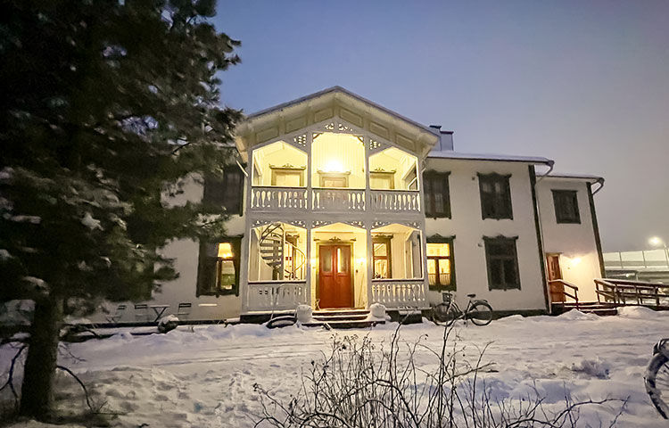 Iltavalaistuksessa oleva kaunis vanha valkoinen rakennus, jossa on erityisen hienot ulkokuistit ylä- ja alakerrassa. Luminen ympäristö.