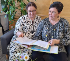 Kaksi naista istuu sohvalla ja tutkii papereita.