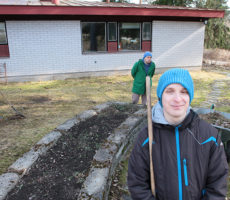 Neljä henkilöä pihatöissä, yksi katsoo kameraan etualalla, muut tekevät töitä taustalla.